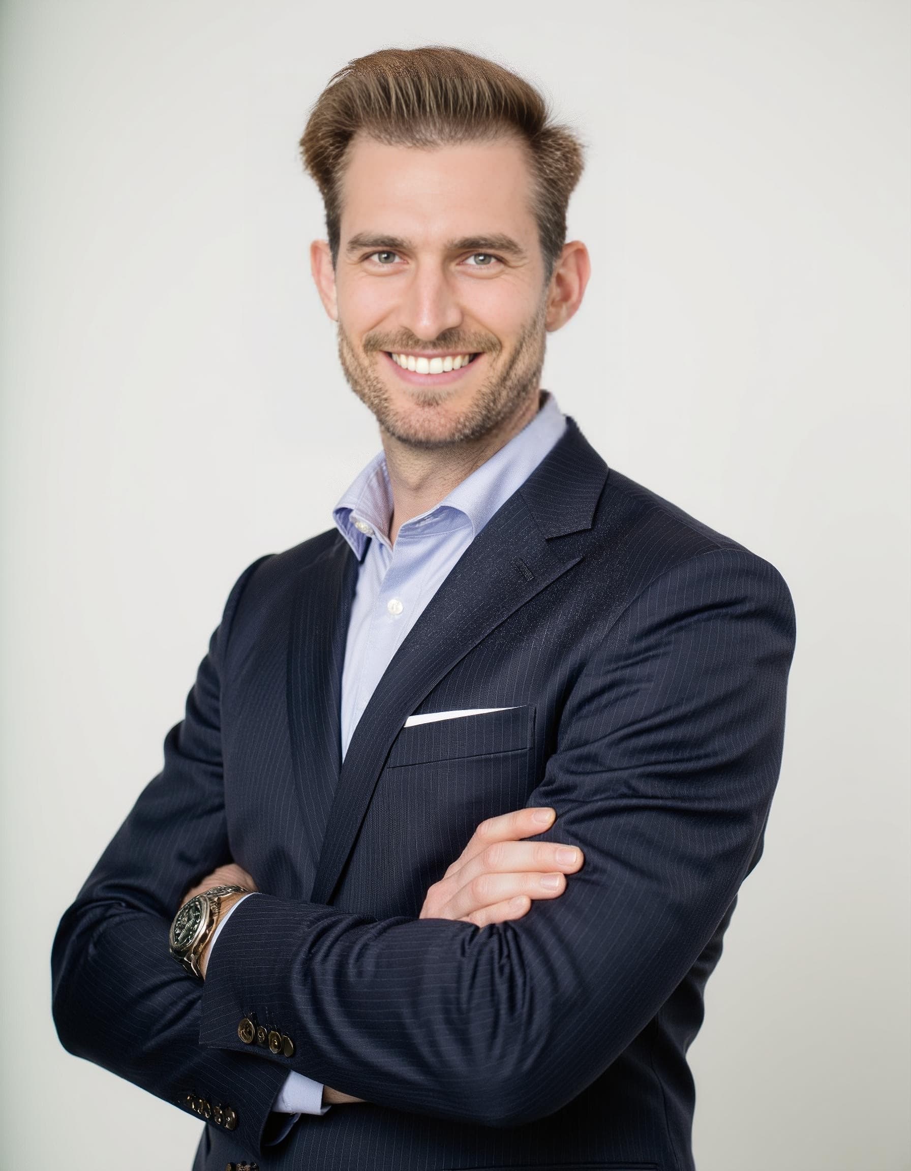 A bearded man in a navy pinstripe jacket and light blue shirt crosses his arms in a studio AI headshot.