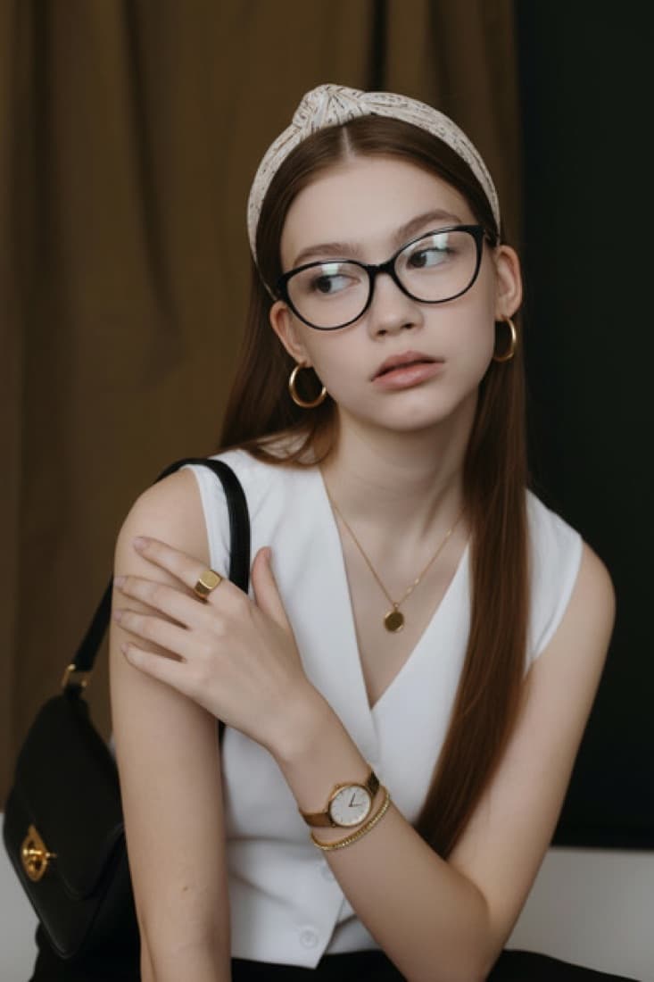 A young woman wears newly added glasses, a headband, gold hoops, and a watch for the Accessory Generator tool.