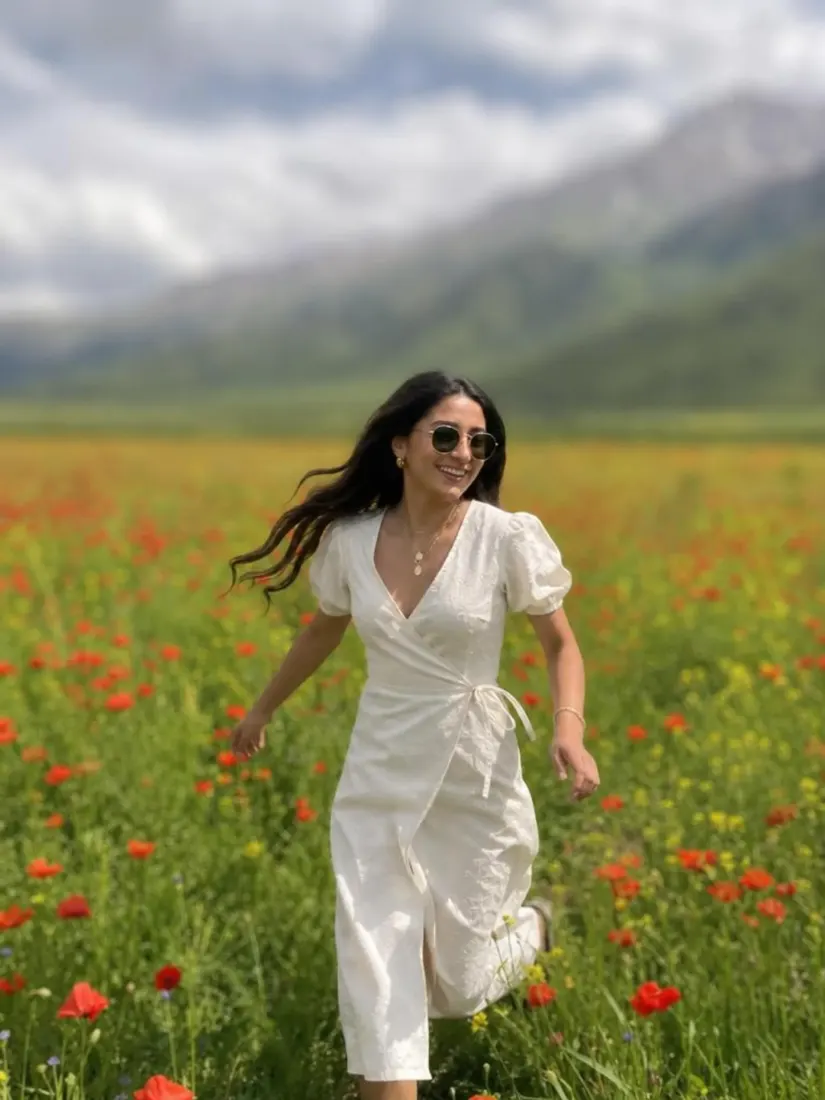 A woman in a white wrap dress runs through a red poppy field with mountains behind her, before the Background Enhancer improves the backdrop.