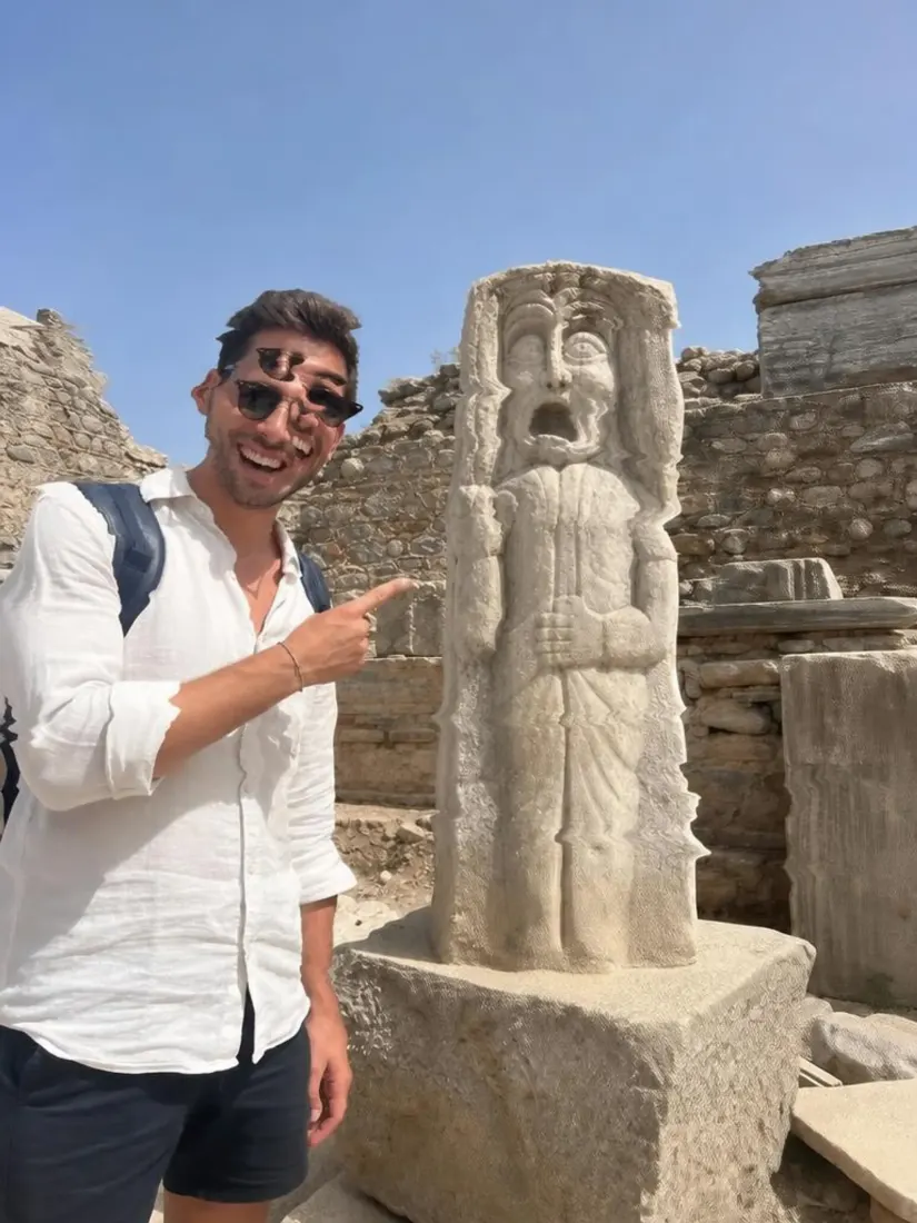 A man in a white shirt points at a stone statue with his face warped, before the Distortion Remover repairs the image.