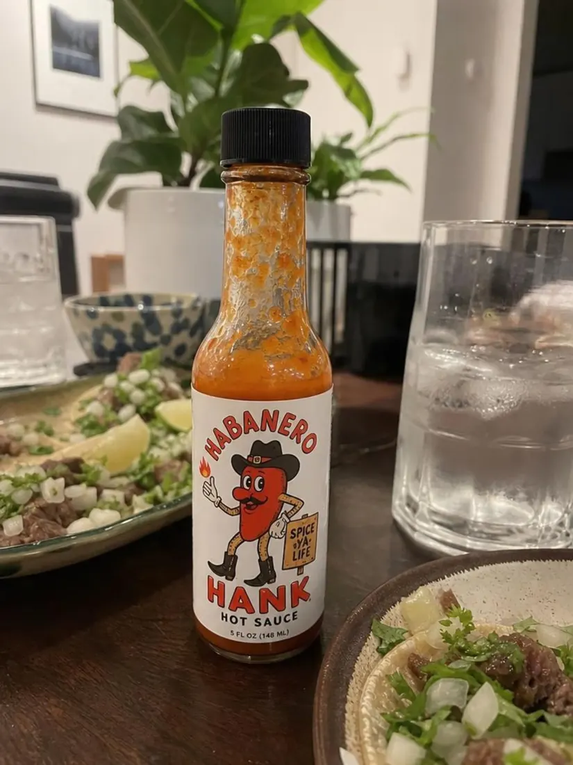 A hot sauce bottle sits plainly on a dining table, before the Product Photo Generator creates a styled ad shot.